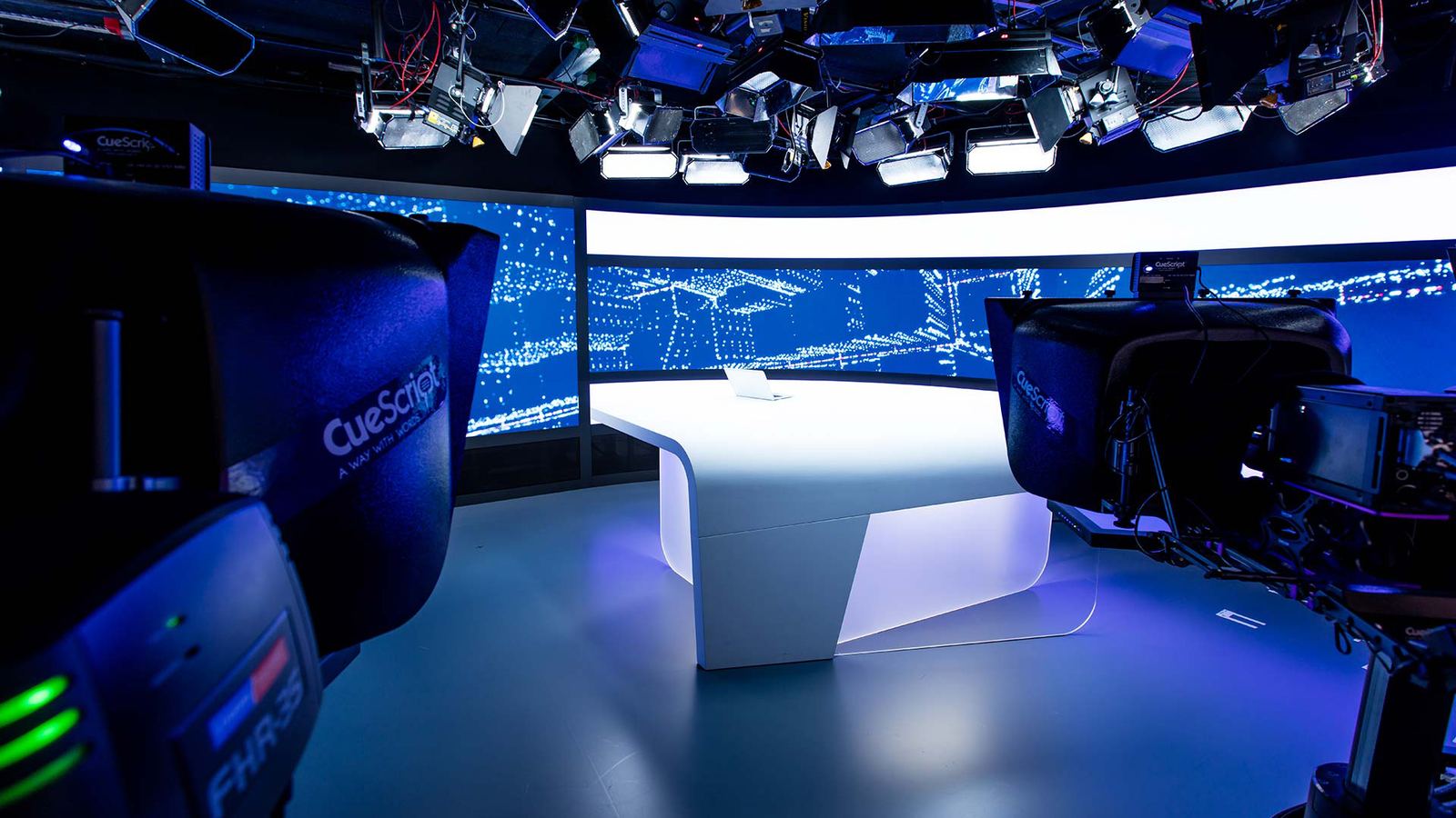 Broadcast studio with a curved TRUE dvLED backdrop behind the presenter desk and studio cameras