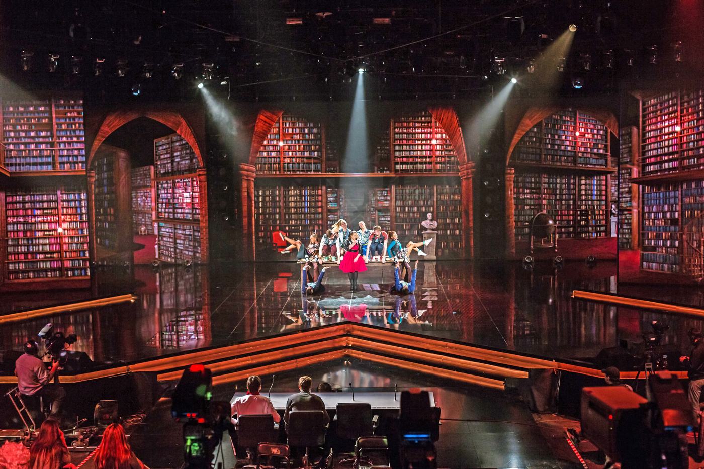 Arched bookshelf walls wrapping a stage in TRUE dvLED, dancers and camera crew at work