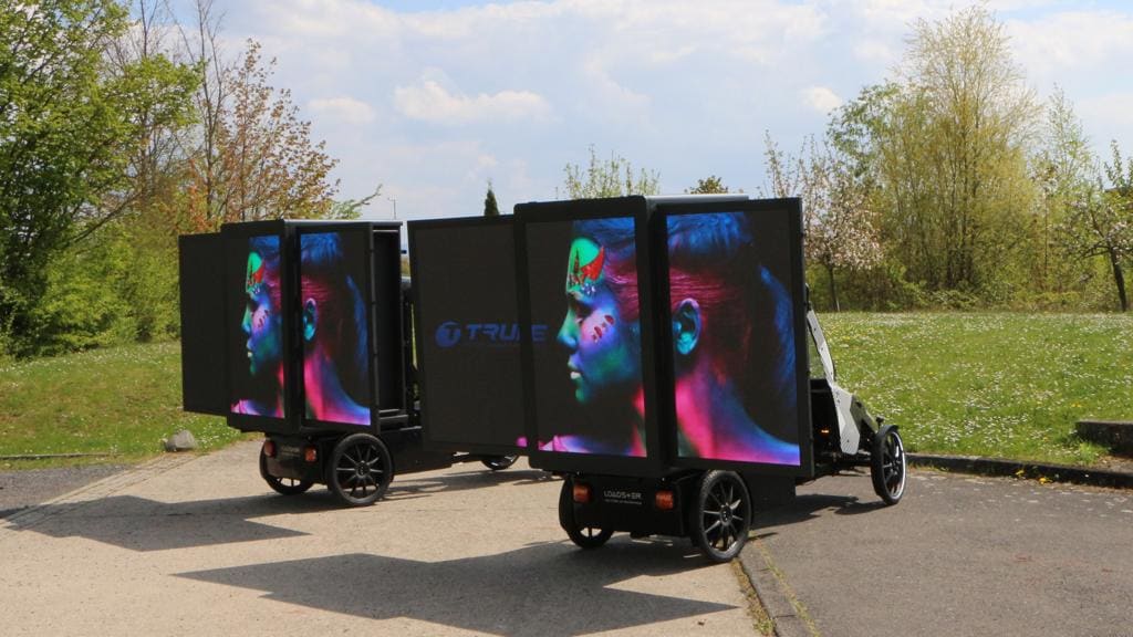 Two TRUE branded mobile dvLED trailers on a daylight path carrying portrait content