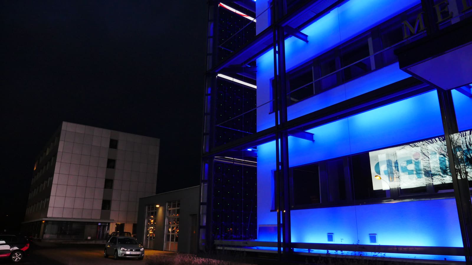 Transparent TRUE LED mesh behind a glass facade lit blue at night