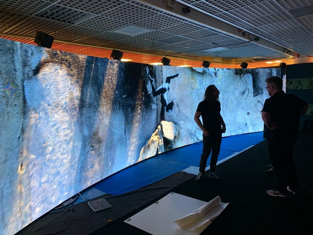 Visitors in front of a large curved TRUE dvLED wall showing a waterfall climber at the Experience Center