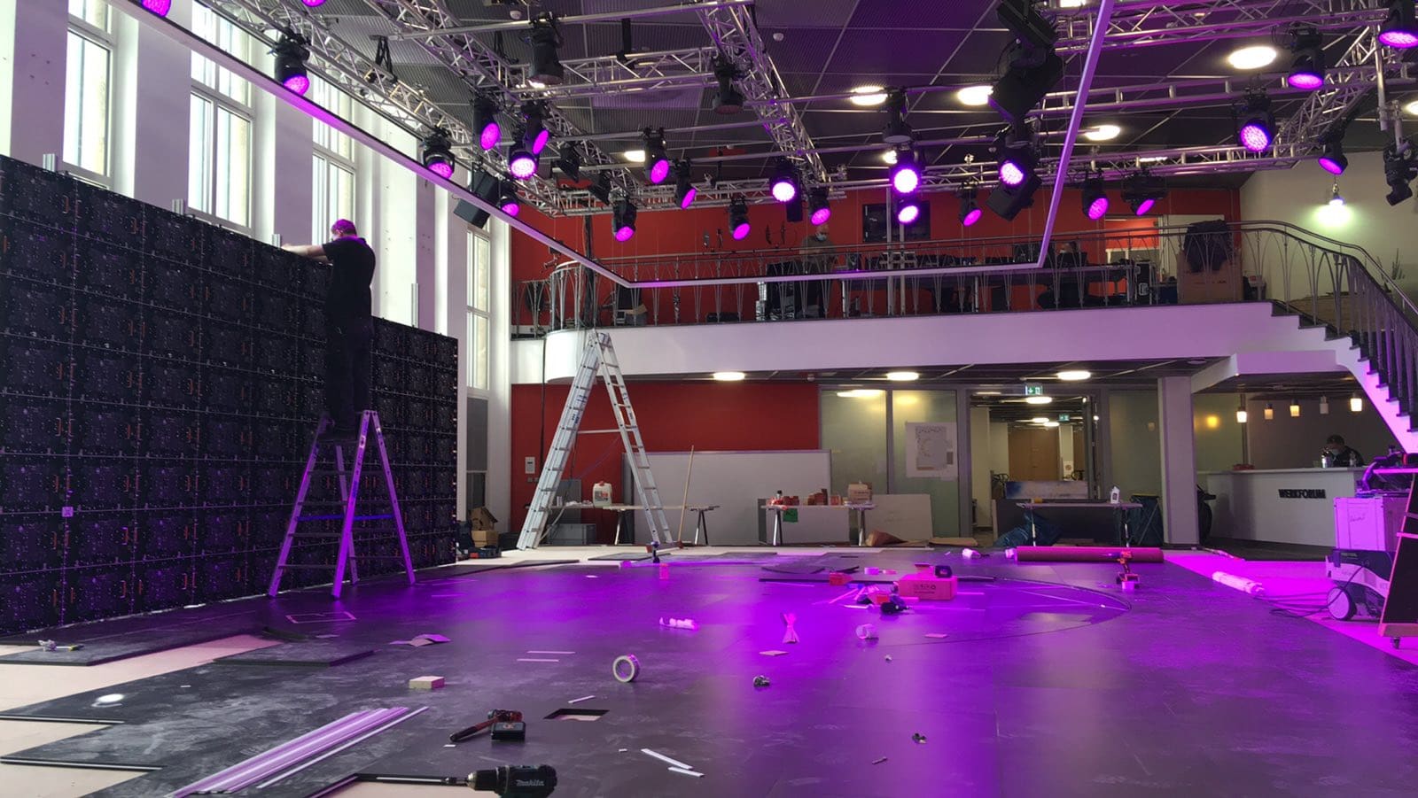 Technician on a ladder installing a TRUE dvLED wall in a venue under stage lighting
