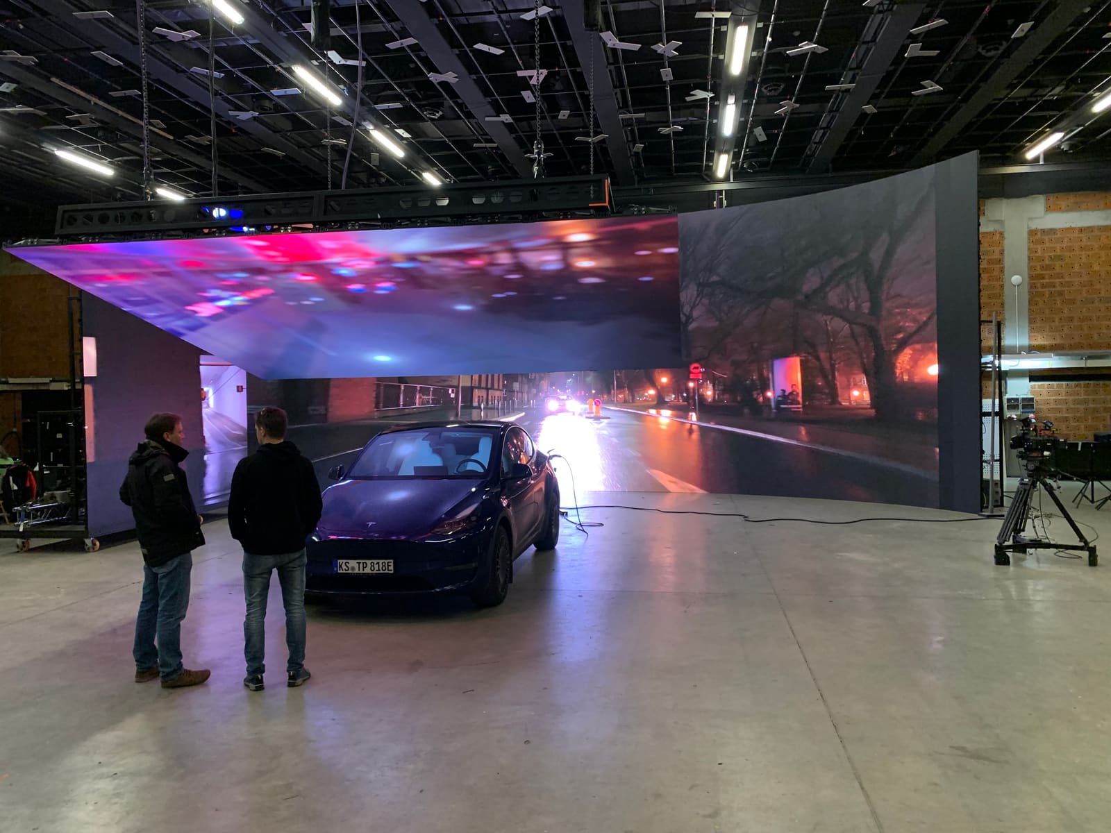 Wet street plate on a TRUE dvLED volume reflecting on the car body, crew watching