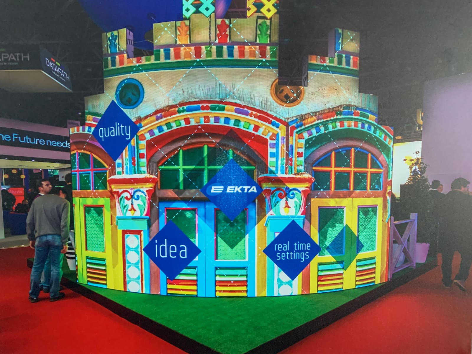 Curved TRUE dvLED wall at a trade show displaying a colorful painted house facade