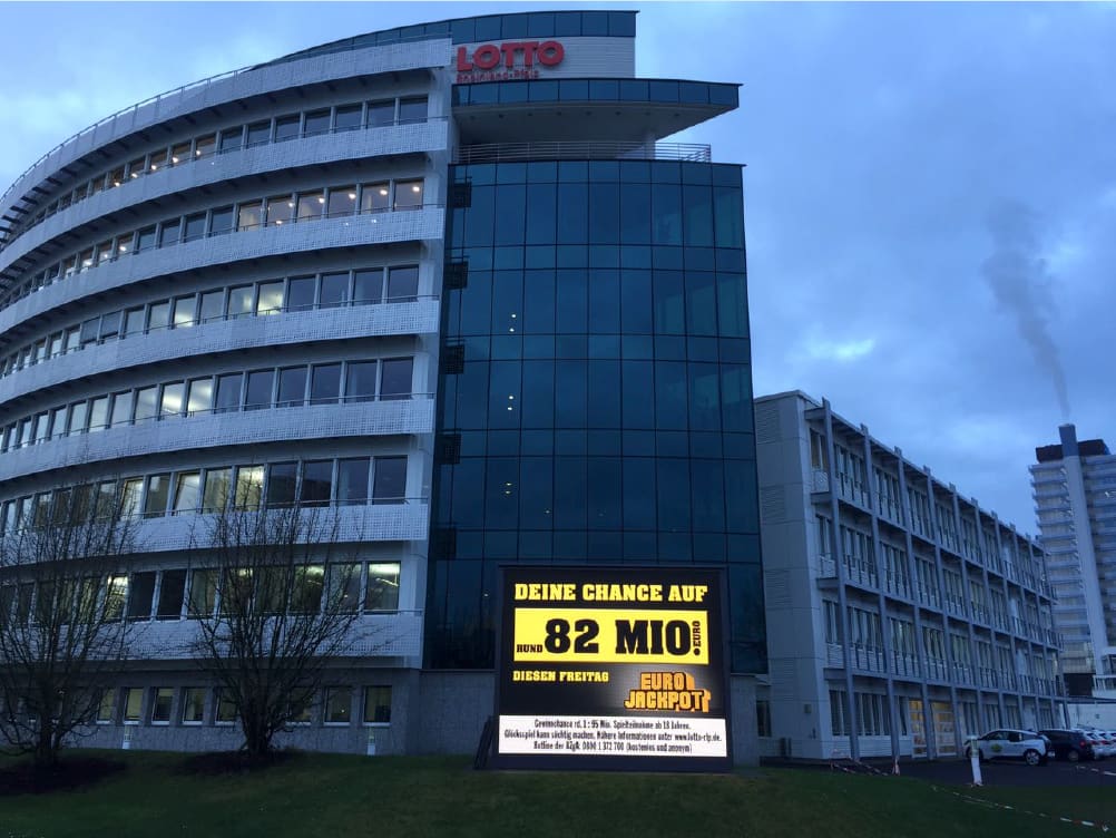 Office building at dusk with a large TRUE dvLED screen advertising a Eurojackpot prize