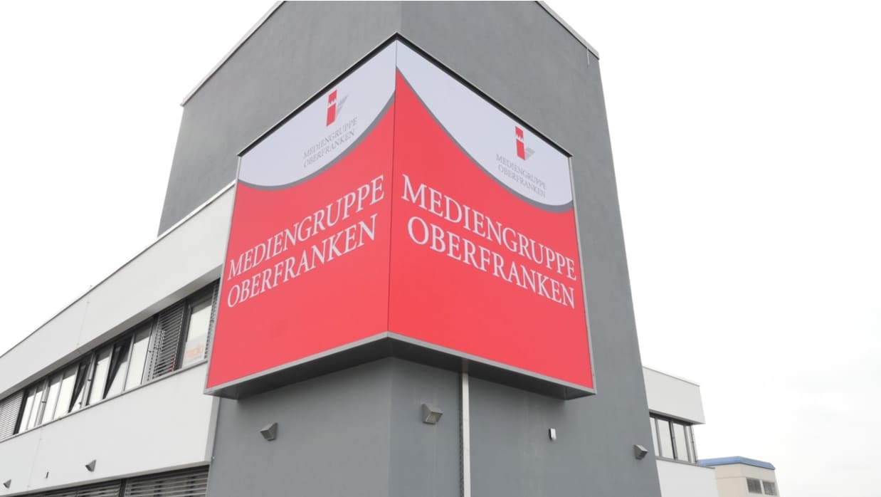 Building tower clad with a red TRUE dvLED display wrapping the corner for Mediengruppe Oberfranken