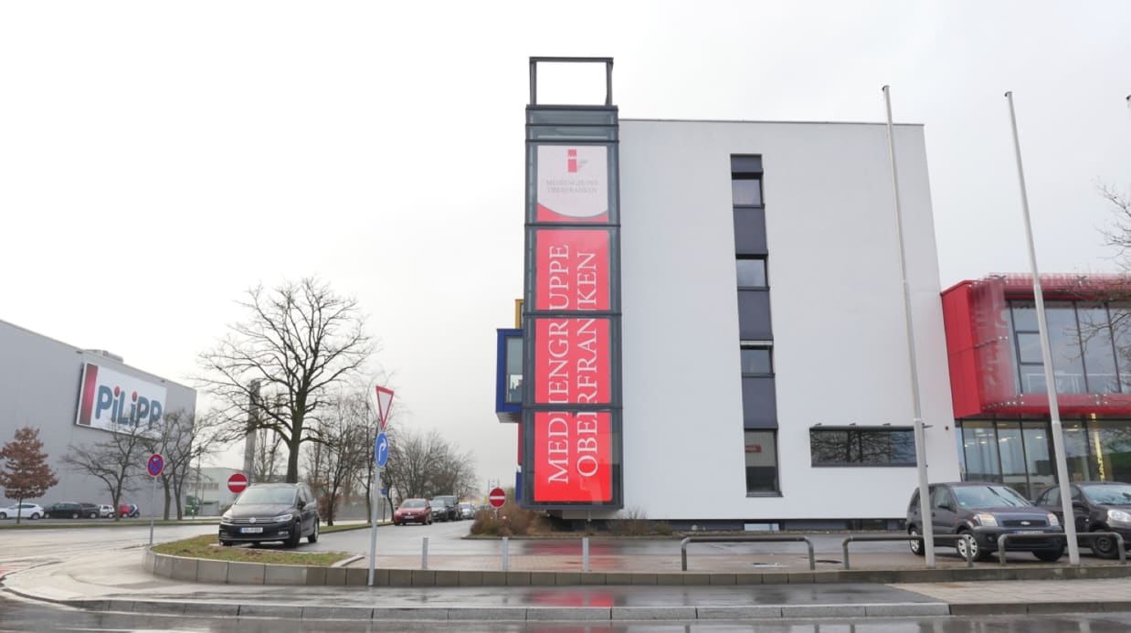 Street view of a tall narrow TRUE dvLED tower display showing red Mediengruppe Oberfranken branding