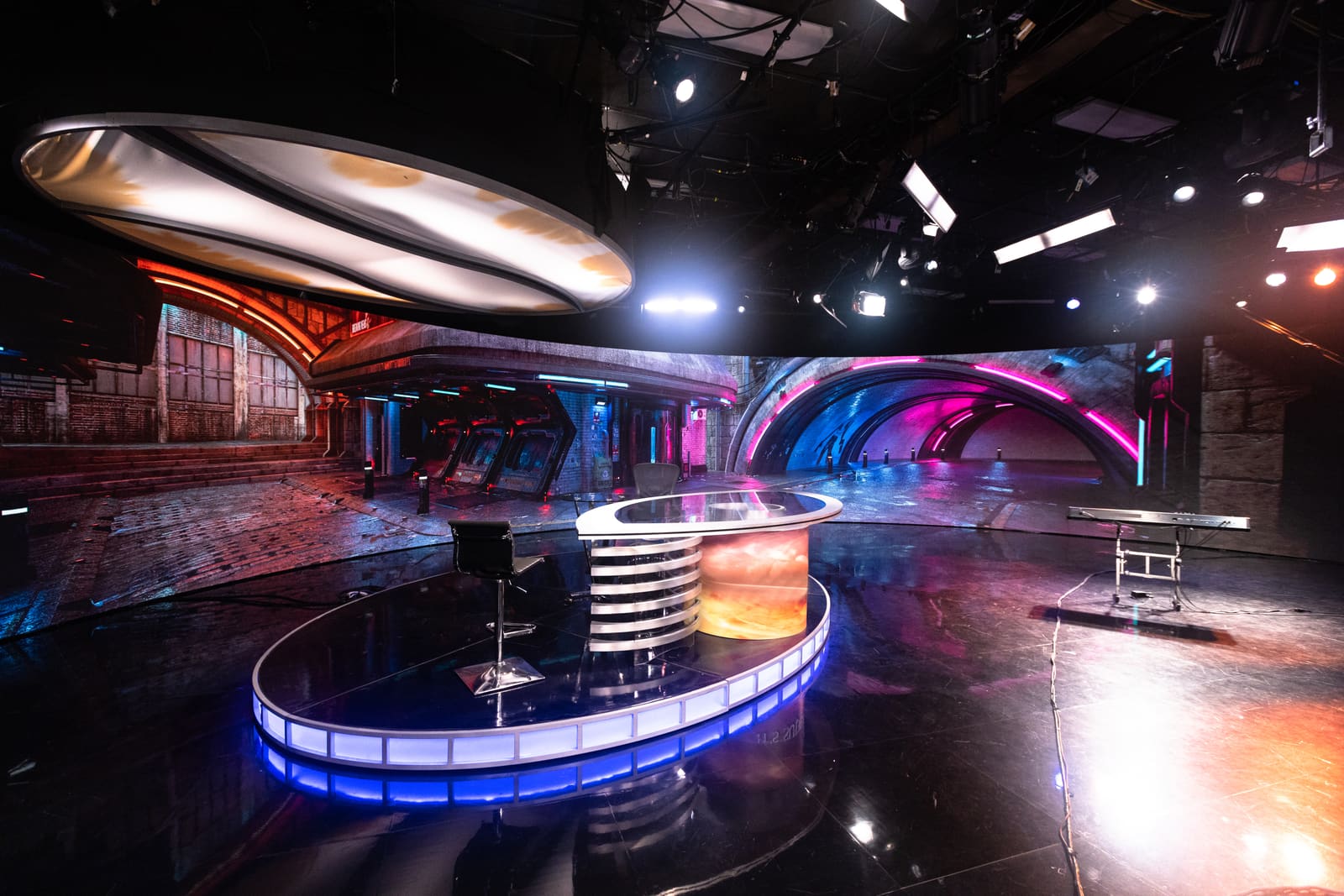 Broadcast studio set with an oval desk in front of a curved TRUE dvLED wall showing a neon subway