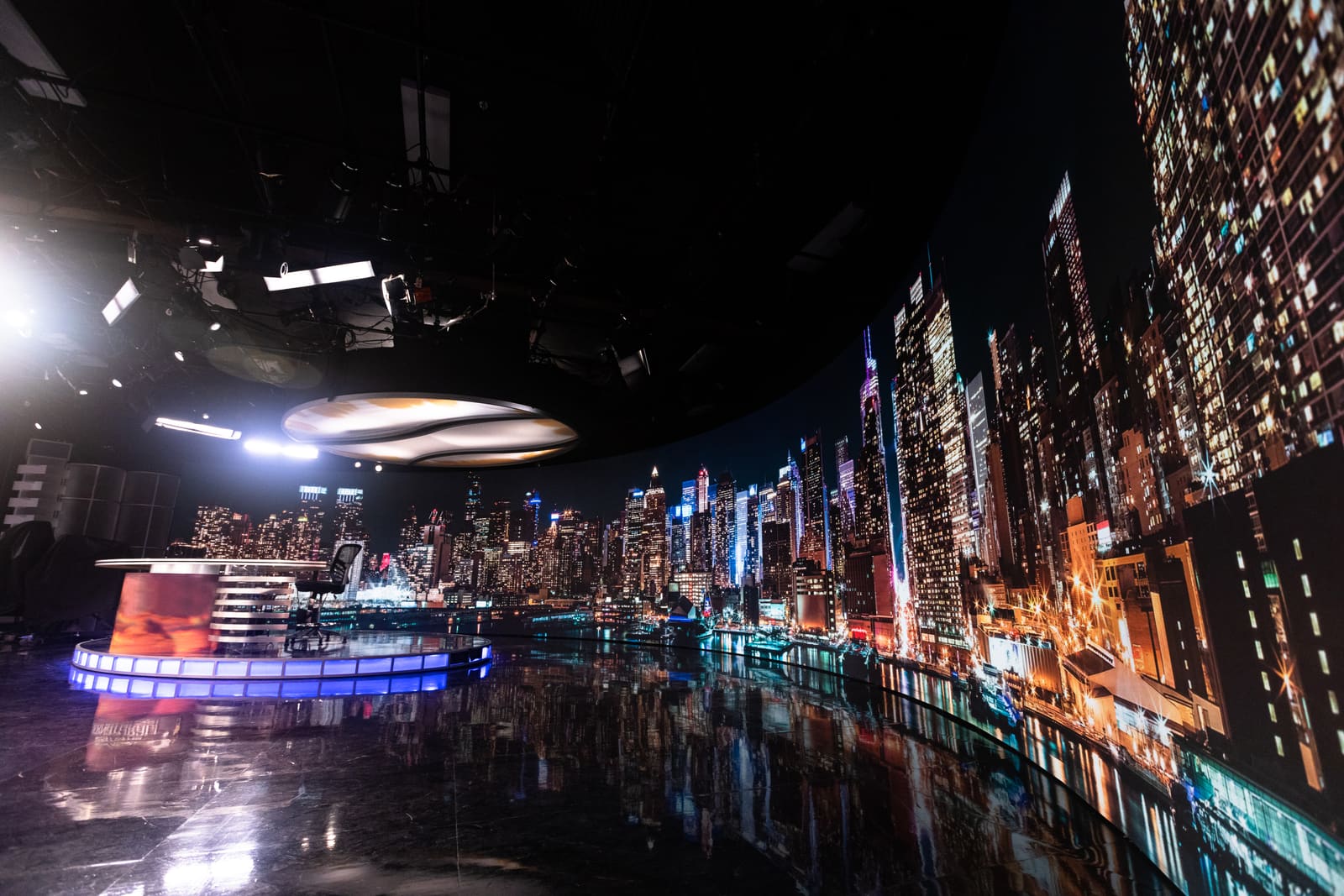 Studio anchor desk beside a large curved TRUE dvLED wall displaying a night city skyline