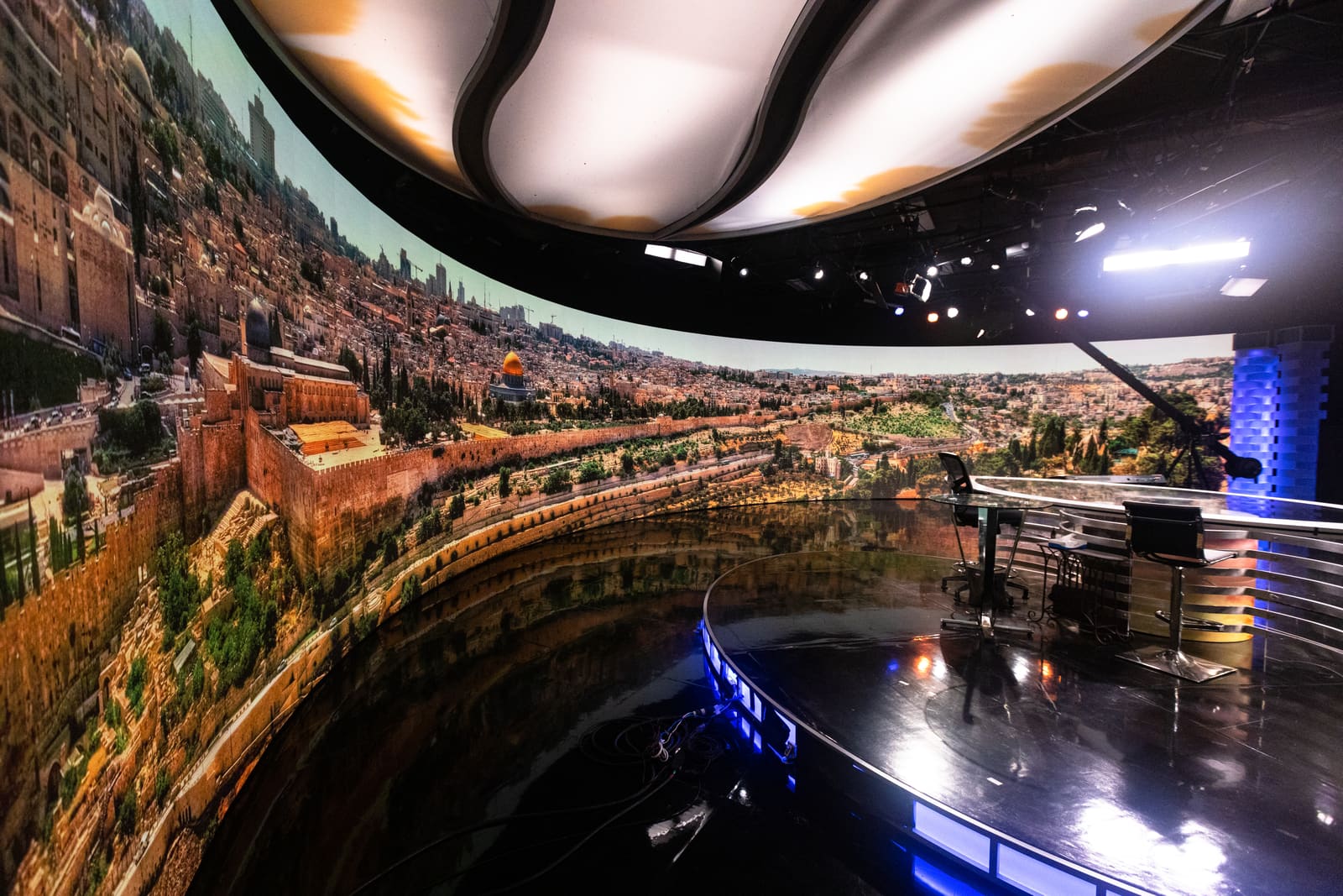 Curved TRUE dvLED studio wall showing a panoramic daylight cityscape behind a glass presenter desk
