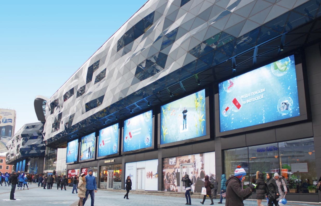 Row of TRUE dvLED screens along a shopping mall facade with shoppers passing on a sunny day