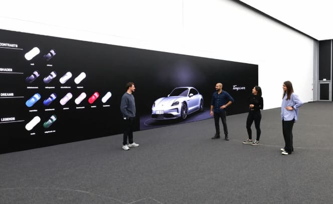Four people beside a long TRUE dvLED wall showing a purple Porsche Taycan and color swatches