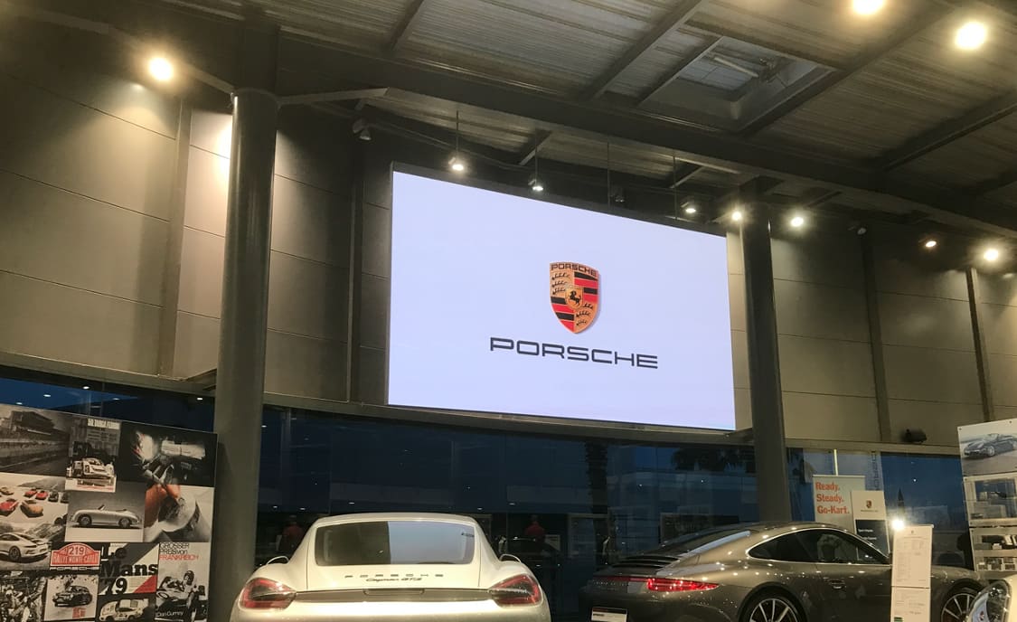 Car showroom with a large TRUE dvLED screen showing the Porsche crest above two parked sports cars