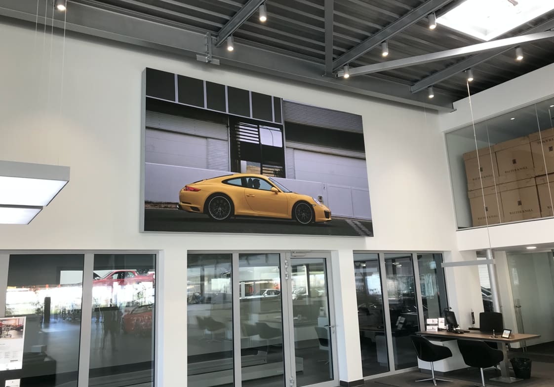 Showroom wall mounted TRUE dvLED display showing a yellow Porsche 911 above glass office doors